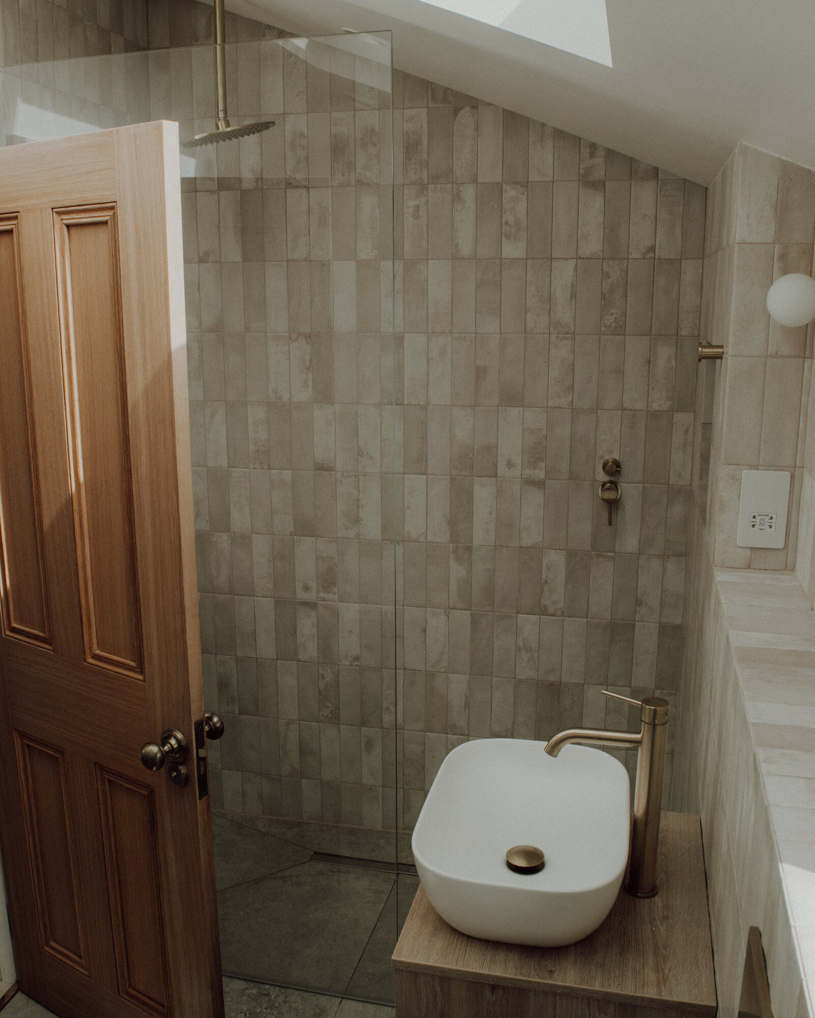Cheltenham: a shower in warm stone tile, with oak door and brass fittings