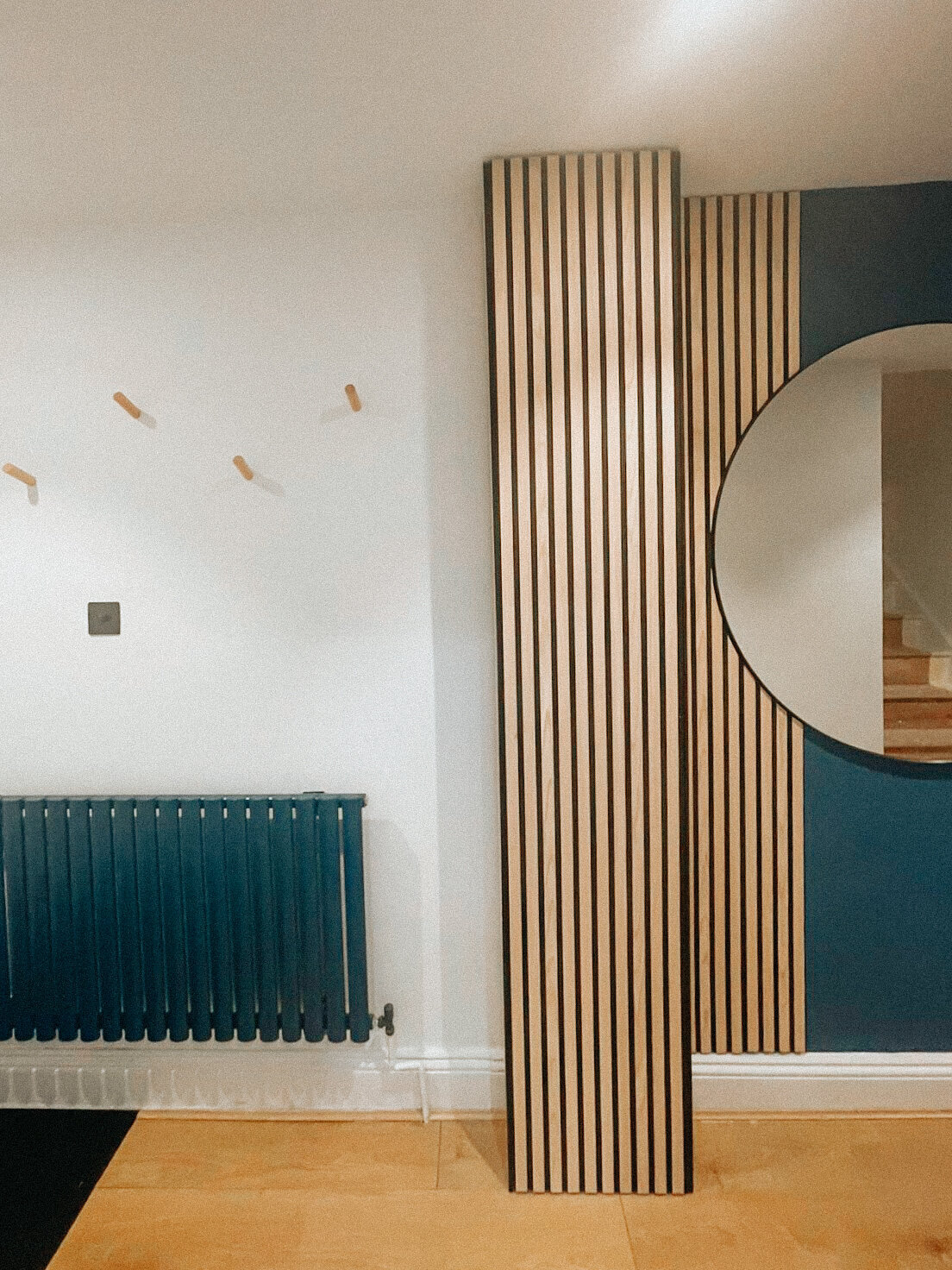 A hall with timber slats, a round mirror and a deep blue wall